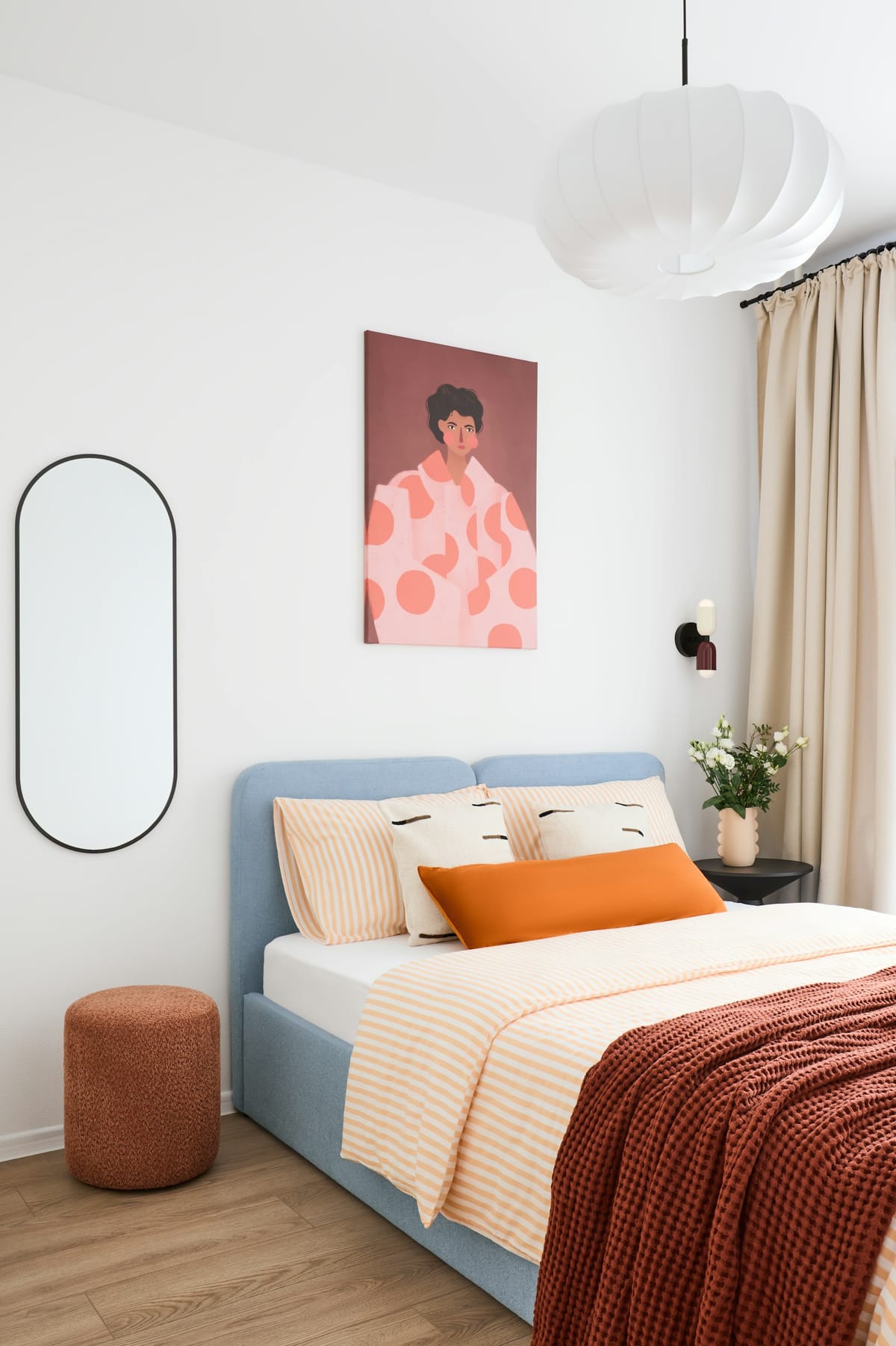 A small, calm bedroom with a pale blue bed, a coral throw, and a pink portrait on the wall